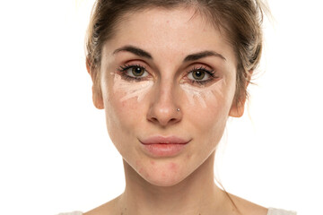 Young woman posing with concealer under her eyes on white background