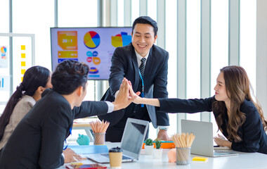 Asian young professional successful male and female businessmen and businesswomen group in formal business suit sitting smiling together holding hands high five each other while agreement deal done