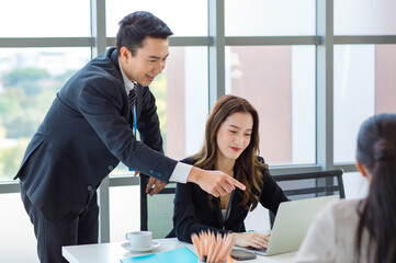 Asian professional successful businessman in formal suit standing showing presenting explaining report investment graph chart data from computer monitor in meeting room to businesswoman colleagues