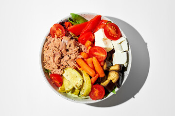 Salad with tuna, vegetables and feta cheese in bowls on a white background. Hard shadows.