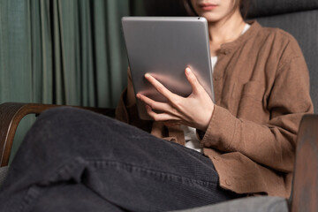 Asian woman holding a tablet is sitting in a rocking chair 