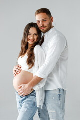 Happy pregnant woman in a studio with her handsome husband wearing bright shirts and smiling