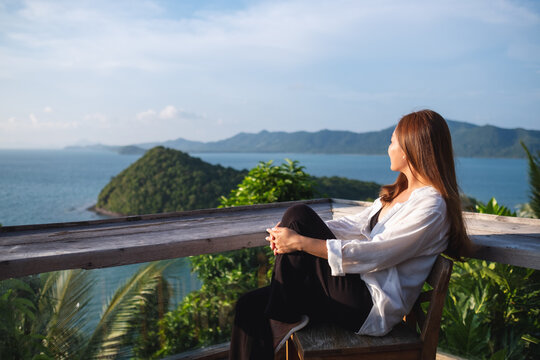 Portrait image of a young asian woman sitting and looking at a beautiful sea view from resort terrace