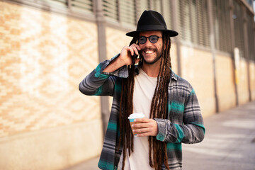 Handsome guy drinking coffee while walking in the street. Modern fashion man using the phone.