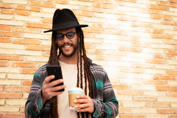 Handsome guy drinking coffee while walking in the street. Modern fashion man using the phone.