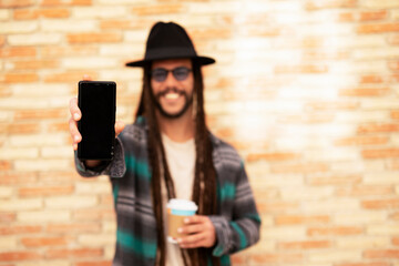 Handsome guy drinking coffee while walking in the street. Modern fashion man using the phone.