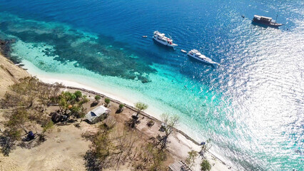 Fototapeta na wymiar Top down drone shot of a paradise island with some boats anchored around in Komodo National Park, Flores, Indonesia. Brownish island turns into white sand beach and further into turquoise and navy sea