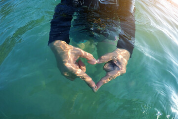 gesture hand in heart shape inside tropical sea with sunny light ray