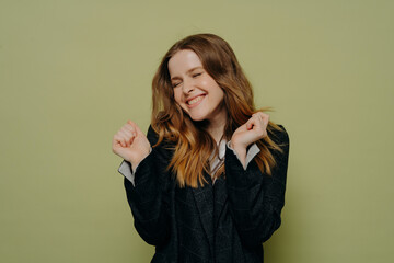 Happy young woman with closed eyes holding hands up with excitement