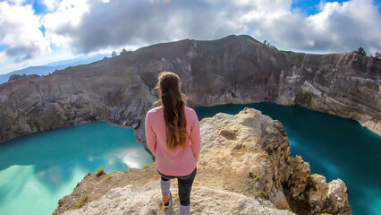 Woman standing at the volcano rim and watching the Kelimutu volcanic crater lakes in Moni, Flores, Indonesia. Woman is relaxed and calm, enjoying the view on lake shining with many shades of turquoise