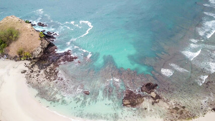 Top-down drone shot of an idyllic Koka Beach. Hidden gem of Flores, Indonesia. Beauty in the nature. Calm waves washing the cliff's slopes. Serenity and calmness. Beach surrounded by high, green hills