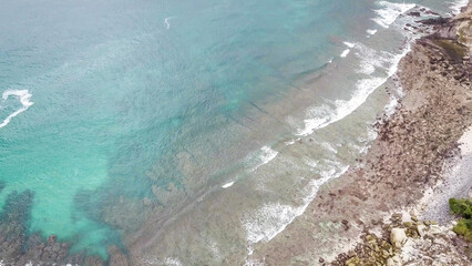 Top-down drone shot of an idyllic Koka Beach. Hidden gem of Flores Indonesia. Beauty in the nature. Calm waves washing the cliff's slopes. Serenity and calmness. There are a lot of boulders in the sea