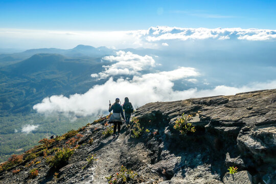 A Couple Walking Down The Steep Side Of Volcano Inierie In Bajawa, Flores, Indonesia. They Are Enjoying The Beautiful View On Volcanic Island. They Walk Down Very Fast, Surrounded By Clouds.