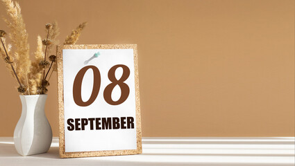 september 8. 8th day of month, calendar date.White vase with dead wood next to cork board with numbers. White-beige background with striped shadow. Concept of day of year, time planner, autumn month