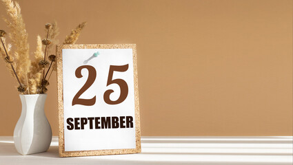 september 25. 25th day of month, calendar date.White vase with dead wood next to cork board with numbers. White-beige background with striped shadow. Concept of day of year, time planner, autumn month