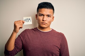 Young handsome latin man celebrating 8th march womens day holding reminder paper with a confident expression on smart face thinking serious