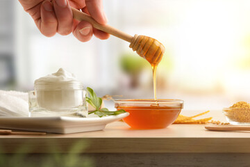 Jar of body moisturizer with honey and hand with stick