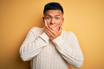 Obraz premium Young handsome latin man wearing white casual sweater over yellow background shocked covering mouth with hands for mistake. Secret concept.