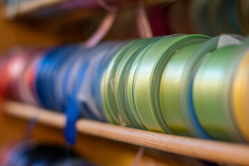 Many colorful ribbons stacked on a shelf to be sold in store, ribbon sale in a shop, creative handcraft or sewing accessories in rolls. Selective focus with shallow depth of field.