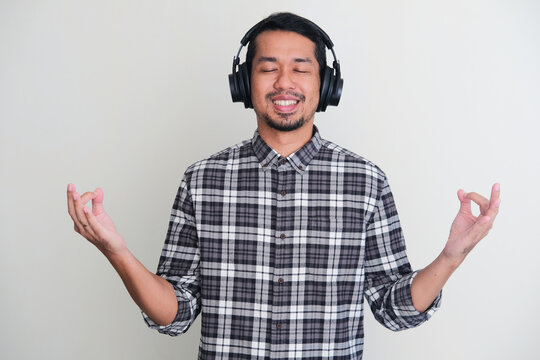 Adult Asian man showing doing meditation pose while enjoying music using headset