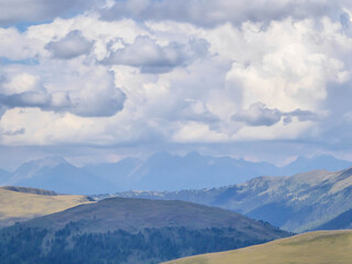 Hiking trails in the high mountain. Green grass and bushes cover the slopes. Endless chains of mountains visible. Thick clouds on the sky. Solo walk allowing for reverie and reflection. Natural beauty