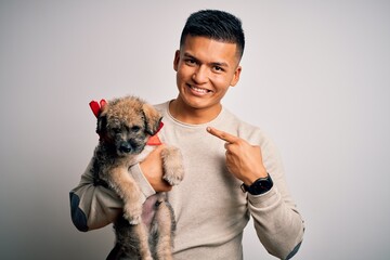 Obraz premium Young handsome latin man holding cute puppy pet over isolated white background very happy pointing with hand and finger