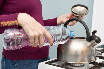 woman pouring clean water from a bottle into a kettle