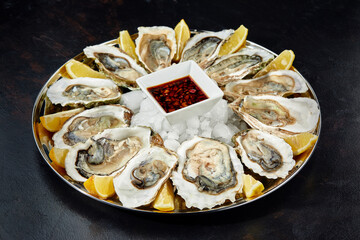 Oysters with lemon served on black round platter. Luxury delicatessen seafood.