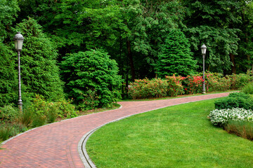 curved pedestrian pavement of stone tiles in park with slope landscape lighting and green plants on...