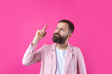 Handsome man with a beard in a pink jacket is thinking over an isolated red background.