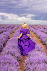 A woman walks in a field of lavender. A girl in a purple dress runs in lavender. Photo from the back