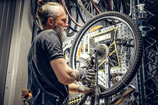 Aged mechanic fixing bicycle wheel in modern workshop
