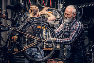 Old man and his grandson fixing bicycles together in repair shop