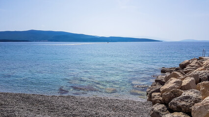 Stony beach in Krk, Croatia. The sea has a turquoise color. Surface of the sea is calm, there are...