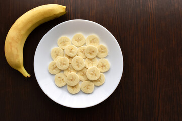 Banana slices on a white plate.  Copy space is on the right side.  Flat lay top view photo.  Food from above concept.