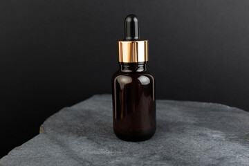 Brown bottle with dropper with a beauty serum on a granite stone on black background. Glass...