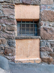 Secured with a sturdy ironwork, the small window stands between the ocher plaster and the stone...