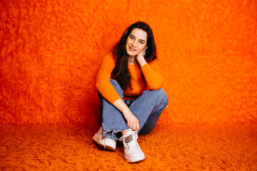 Portrait of brunette caucasian young woman with long hair, sitting against an orange haired background