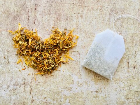 Herbal tea bag next to calendula (marigold) tea leaves in a heart shape