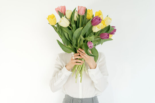 Woman holding a bunch of multi coloured tulips in front of her face
