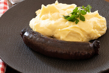 close up of cooked black pudding with mashed potatoes in a plate on a table