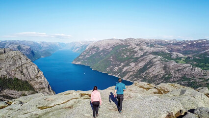 Couple sitting on a rock and admiring a view on Lysefjorden. Areal shot, upper perspective on the couple. Endless view of the fjord. Couple rising hands above their head and forming a heart. Freedom