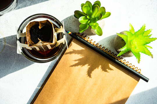 Overhead view of a glass of coffee, individual coffee filter, notepad and houseplants