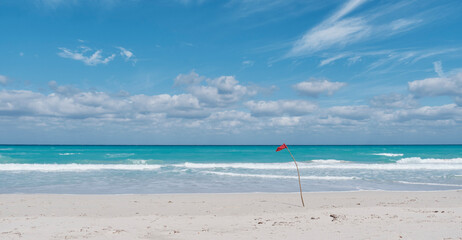 Fototapeta na wymiar Red flag on sandy beach of Atlantic Ocean, Varadero, Cuba. Danger sign, no swimming.
