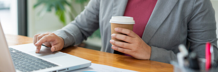 Business analyst concept the female officer holding a cup of coffee typing information on the computer laptop