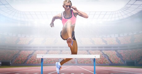 Composite image of caucasian female athlete jumping over hurdles against sports stadium
