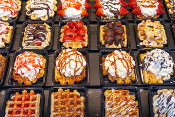 Delicious traditional Liege waffles with colorful toppings on display in a store window in Brussels, Belgium. Sugary desserts. Typical Belgian sweet food.