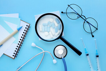medical mockup, pharmaceutical pills, tablets, capsules under a magnifying glass on a pastel blue...