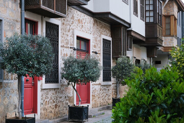 Beautiful facade of an ancient house made of stones and concrete with red entrance doors and balconies, with trees in potted flower beds at the entrance