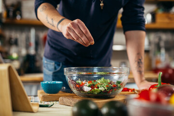 man seasoning salad in his kitchen